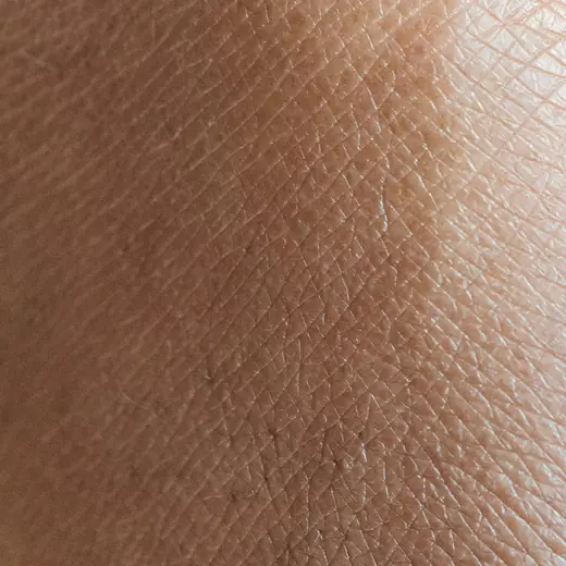 Nahaufnahme von Hautstruktur mit feinen Linien und Poren im Tageslicht.