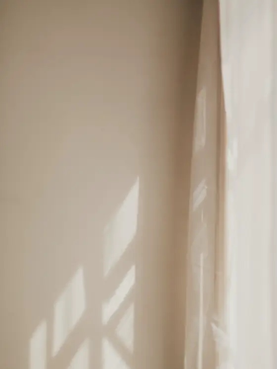 Leinenvorhang vor einem Fenster, Tageslicht zeichnet ein Kreuz auf den Stoff.